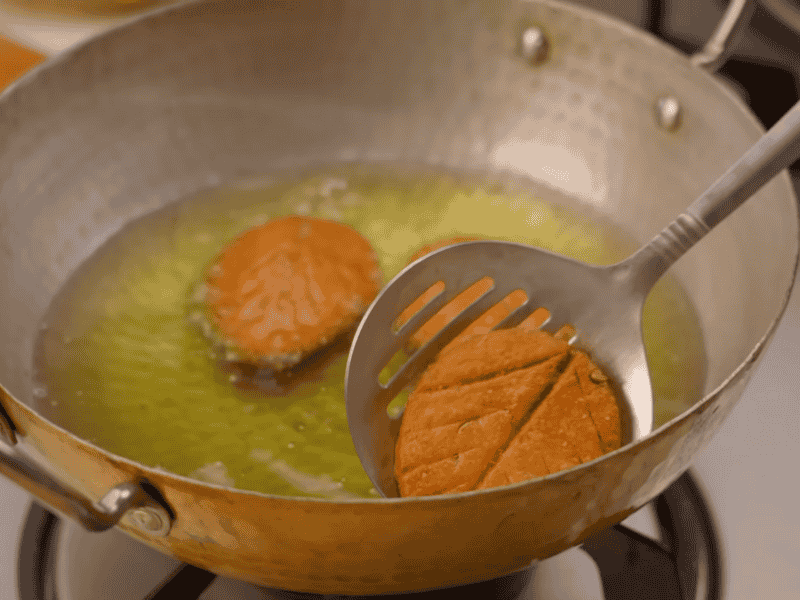 Deep frying Thekua in ghee until golden brown"